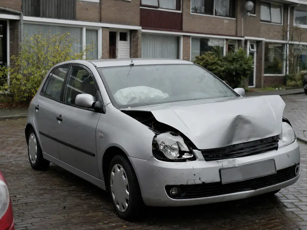 Zilveren hatchback met een ingedeukte voorkant en een geknapt koplampglas voor rijtjeshuizen